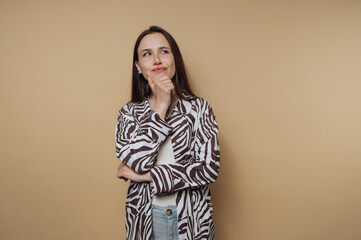 Thoughtful woman in zebra-patterned jacket poses with a smile against a beige background in a...