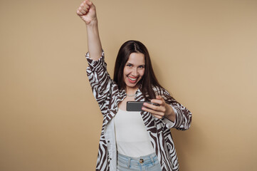 Excited young woman celebrates while taking selfie against a simple beige background