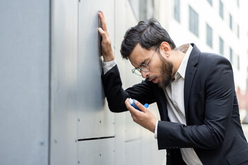 A man in formal attire uses an asthma inhaler while leaning against an outdoor wall, conveying a...