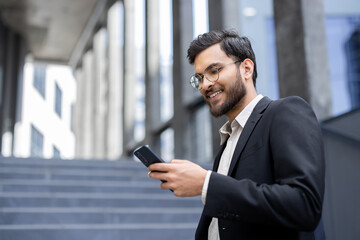 A professional male in a suit and glasses engaging with his phone outdoors, exuding confidence and...
