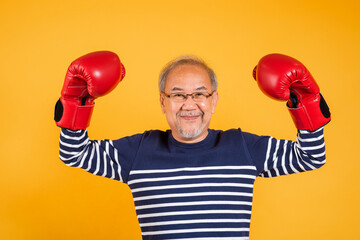 Portrait Asian old man wearing glasses wear two red boxing gloves studio shot isolated yellow...