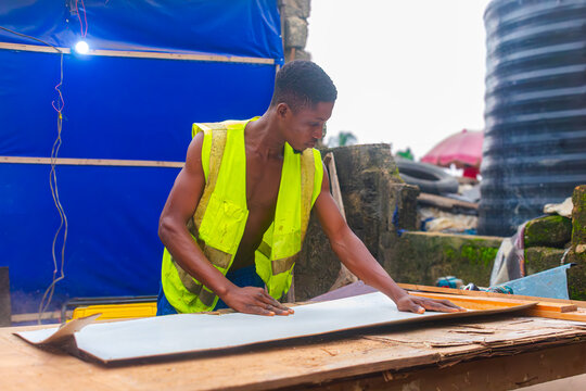 Young African carpenter standing, cutting wooden board