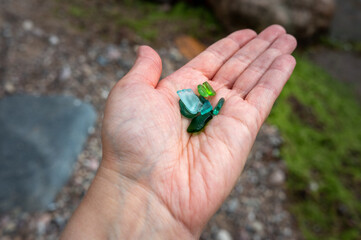 A handful of smooth, green and turquoise sea glass sits in the palm of a person's hand.