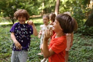 Fototapeta premium Cute little kids having fun with soap bubbles in park, selective focus