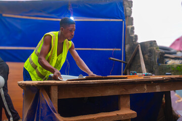 Young African carpenter standing, cutting wooden board