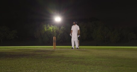 After bowler delivering, diverse teammates blocking and collecting ball on night pitch, copy space