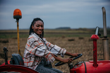 Young female farmer driving red tractor in field after harvesting