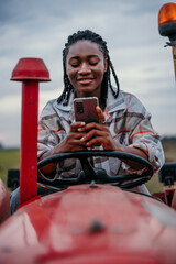 Young female farmer using smartphone on tractor in field