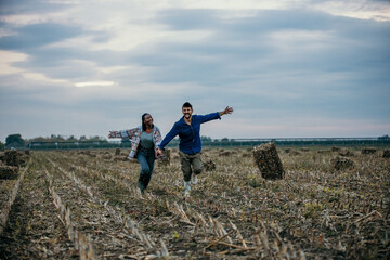 Happy farmers running through harvested field holding hands