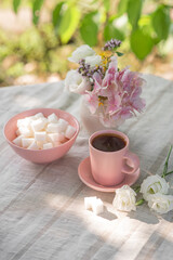 Coffee in a small pink cup with a saucer and a bowl with refined sugar on a table in a summer garden
