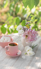 Coffee in a small pink cup with a saucer and a bowl with refined sugar on a table in a summer garden