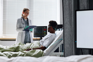 Cheerful Caucasian doctor wearing lab coat holding clipboard with medical record asking questions...