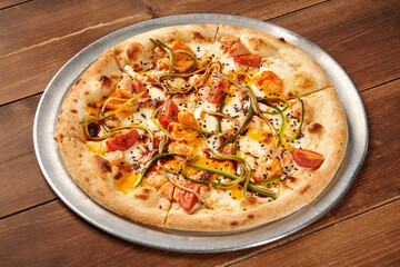 Delicious pizza with salmon, cucumber, tomato and sesame seeds resting on wooden table