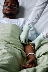 Vertical shot of young Black patient lying in hospital bed with eyes closed getting intravenous...