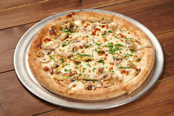 Delicious pizza with mushrooms, white creamy sauce and parsley resting on metal tray on wooden table