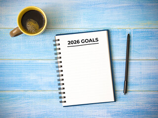Top view of notebook handwriting goals for 2026 year, cup of coffee on blue wooden table. Business plan concept.