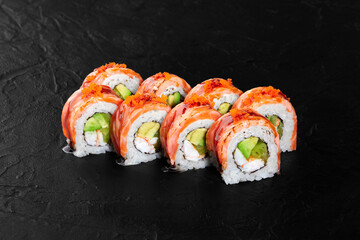 Delicious uramaki sushi rolls with salmon, avocado, and tobiko on black background