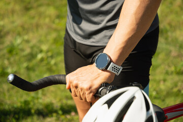 Close up of cyclist hands with smartwatch . Relax with bike at city park.