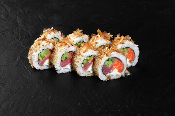 Sushi rolls covered with dried bonito flakes lying on black stone background
