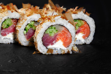 Delicious uramaki sushi rolls with tuna, salmon, cucumber and cream cheese on black background