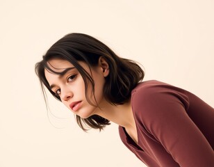 Fototapeta premium Portrait of a young woman with short dark hair wearing a maroon shirt against a light background looking down