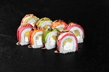 Rainbow uramaki sushi rolls with tuna, salmon, avocado, cream cheese and sesame seeds on black background
