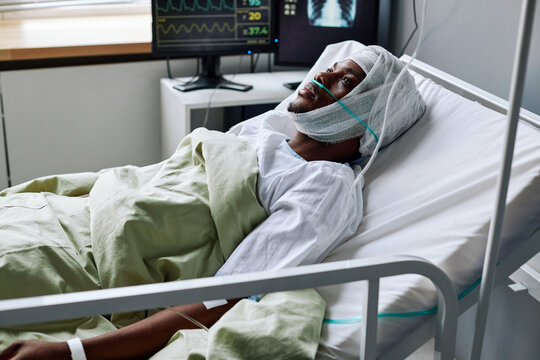 Horizontal shot of young Black man with nasal cannula and bandage on head lying in hospital bed after injury or surgery
