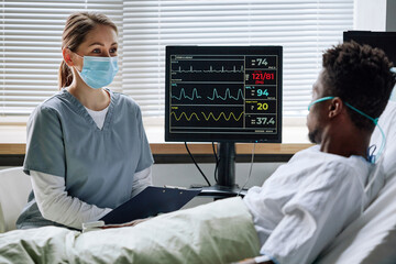 Unrecognizable woman working as doctor in hospital sitting in front of injured man speaking about...