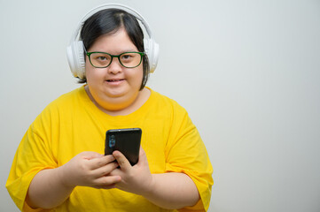Young woman with Down syndrome wearing green glasses and headphones, smiling while holding...