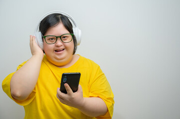 Smiling young Asian woman with Down syndrome wearing yellow shirt and white headphones, holding...