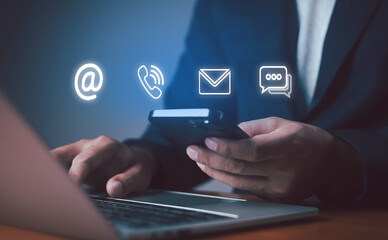 Businessman using smartphone and laptop with communication icons for email, phone, and chat, representing online contact, customer service, and digital business communication.