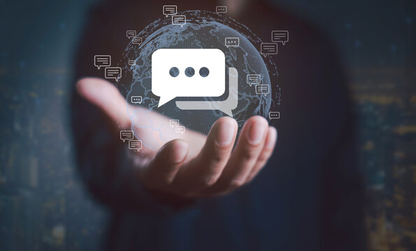 Businessman holding a digital globe with chat bubble icons, symbolizing global communication, online messaging, social networking, and worldwide digital connectivity. - Powered by Adobe