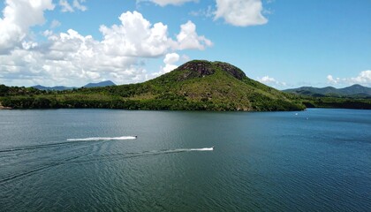 Speedboats carve wakes across vast blue lake toward lush green mountain under bright summer sky