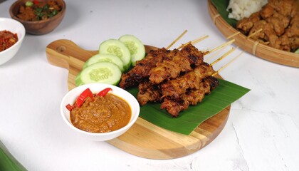 Delicious chicken satay skewers with peanut sauce and fresh cucumber slices on a wooden board
