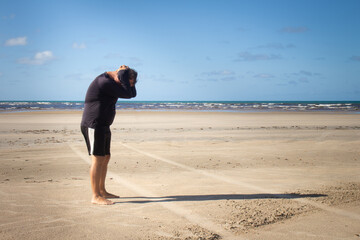 Man standing on beach with hands on head looking down.