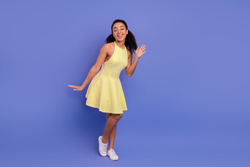 Young cheerful woman in a yellow dress posing against a violet background, showcasing vibrant...