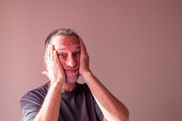 Mature man making funny face with hands on cheeks.