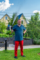 A focused senior man in blue polo shirt and red pants diligently waters his green garden with spray...