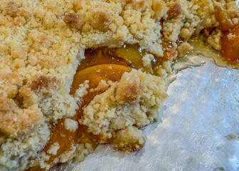Peach crumble pie cut with peaches and juice showing on a silver pan