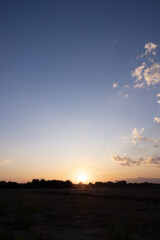 Vertical composition image of sun sky and clouds at evening time. Blue orange and yellow color tone. Silhouette with mountain and forest. Suit for nature background.