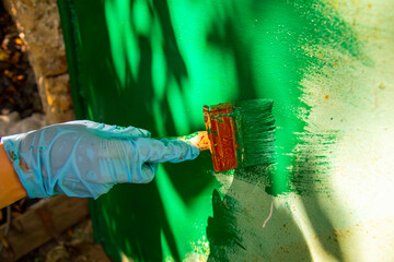 A person in blue gloves painting a green wall with a brush