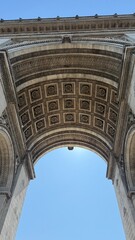 Paris, France - July 4 2025: View from beneath the Arc de Triomphe showing the detailed coffered ceiling and stone arch against a clear blue sky.