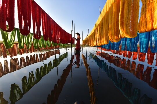 Side view of a woman standing amongst rows of colourful lotus threads hanging at Inle Lake, Myanmar