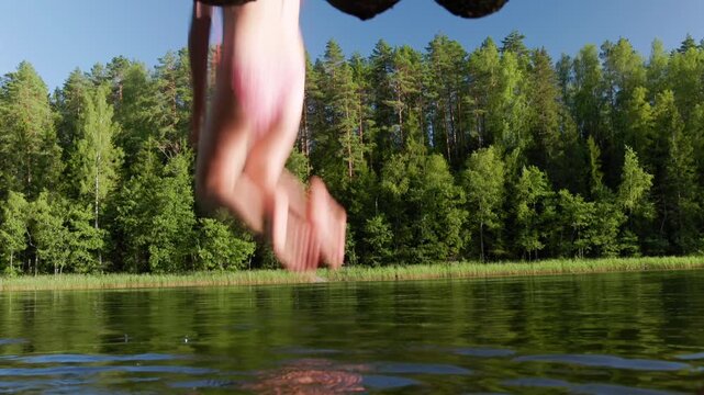 Young girl in a swimsuit leaps from a rustic wooden pier into a forest lake, creating a big splash on a bright summer afternoon surrounded by nature