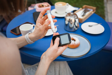 Close-up of a woman with type 1 diabetes checking her blood sugar level with a finger prick test before having a coffee and pastry at a cafe