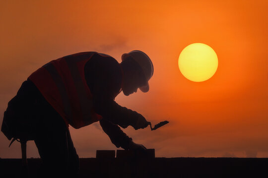 Side view silhouette of a bricklayer laying bricks on a construction site at sunset, Thailand