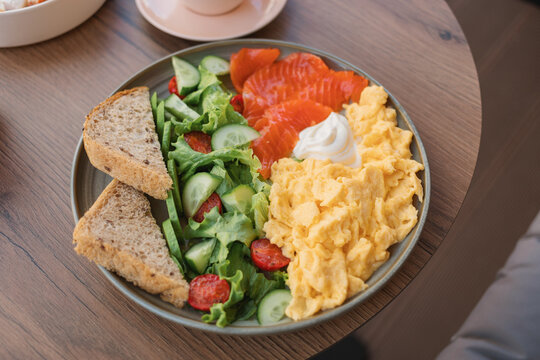 Overhead view of a plate of scrambled eggs, smoked salmon, mixed salad, multigrain bread and cream cheese on a table