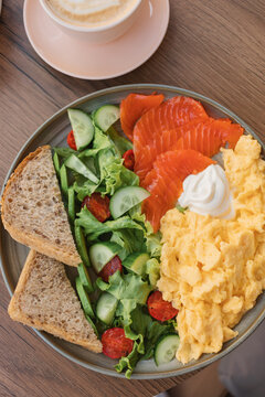 Overhead view of scrambled eggs, smoked salmon, mixed salad, multigrain bread and cream cheese with a latte coffee