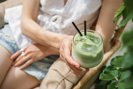 Close-up of a mid adult woman sitting outdoors in summer drinking an iced matcha latte