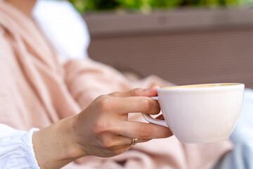Close-up side view of a woman sitting outdoors drinking a cup of coffee